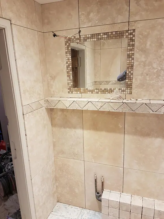 Stone-effect tiling going up, with a mosaic-framed mirror recess set into the wall.