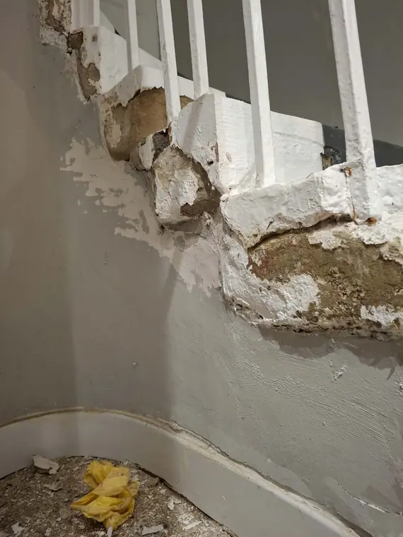 Broken plaster along the stair string, knocked and crumbled back to the backing.