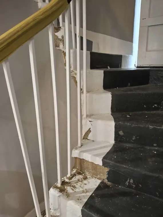 The staircase before repairs, with the plaster edge along the treads cracked and falling away.
